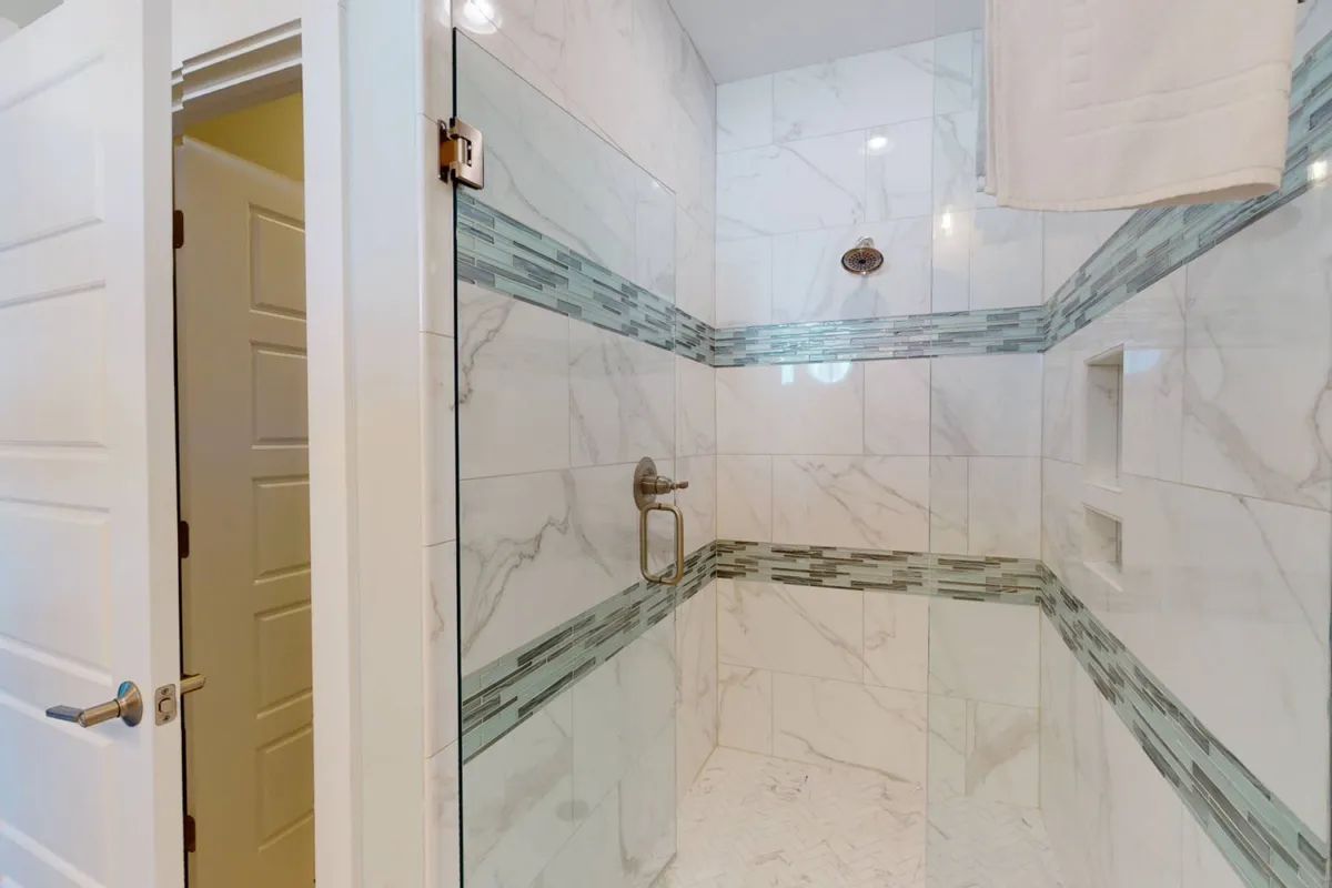 A modern bathroom showcasing a marble-tiled walk-in shower with a glass door and a decorative tile accent. The space feels crisp, clean, and spa-like, reflecting attention to detail in the en-suite or hall-adjacent bathrooms.