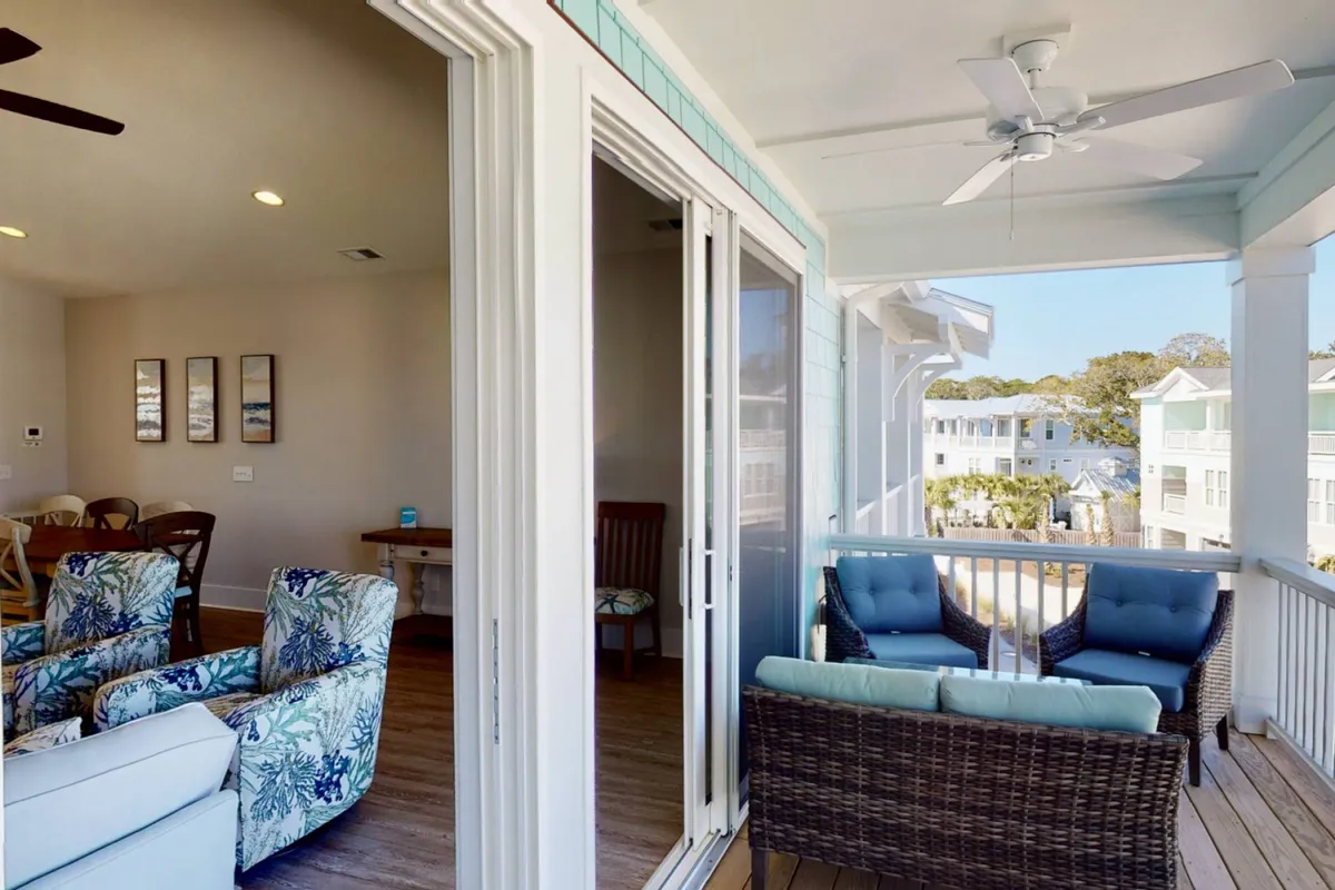 A welcoming covered deck area with comfortable outdoor seating, decorative wall art, and views of the surrounding neighborhood houses. The setting is staged for relaxation or small gatherings, with soft lighting and an inviting atmosphere.