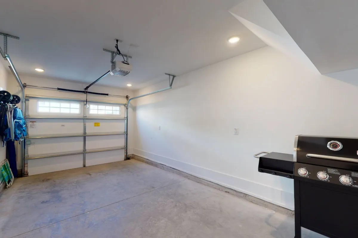 A practical view of the garage area with the garage door visible and a grill in the foreground. The space is organized, hinting at storage possibilities for beach gear such as chairs and a beach wagon.
