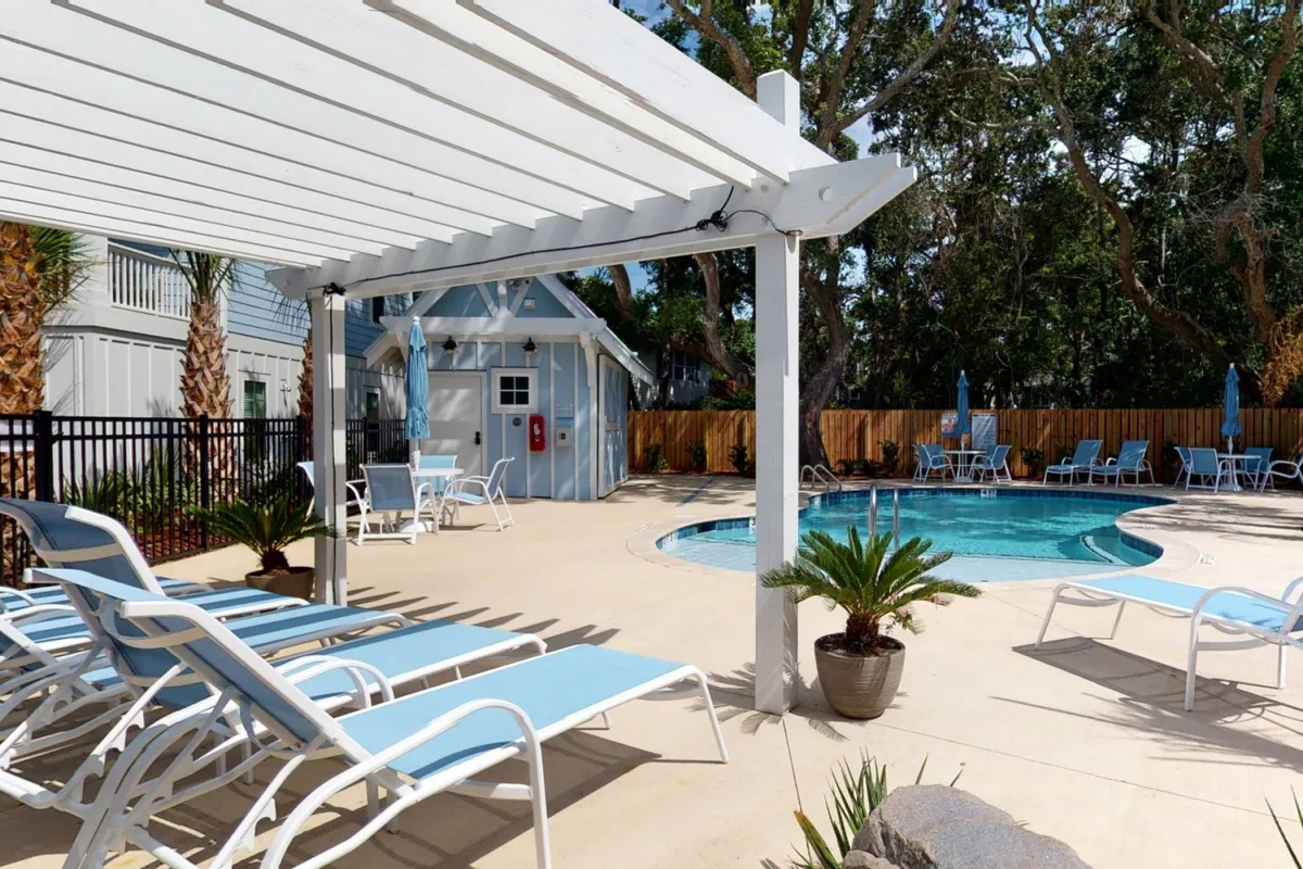 This image features a tranquil swimming pool surrounded by lounge chairs, a pergola for shade, and lush greenery. The pool is clean and modern, evoking the feel of a resort's exclusive amenity space, ideal for socializing or relaxing on sunny days.