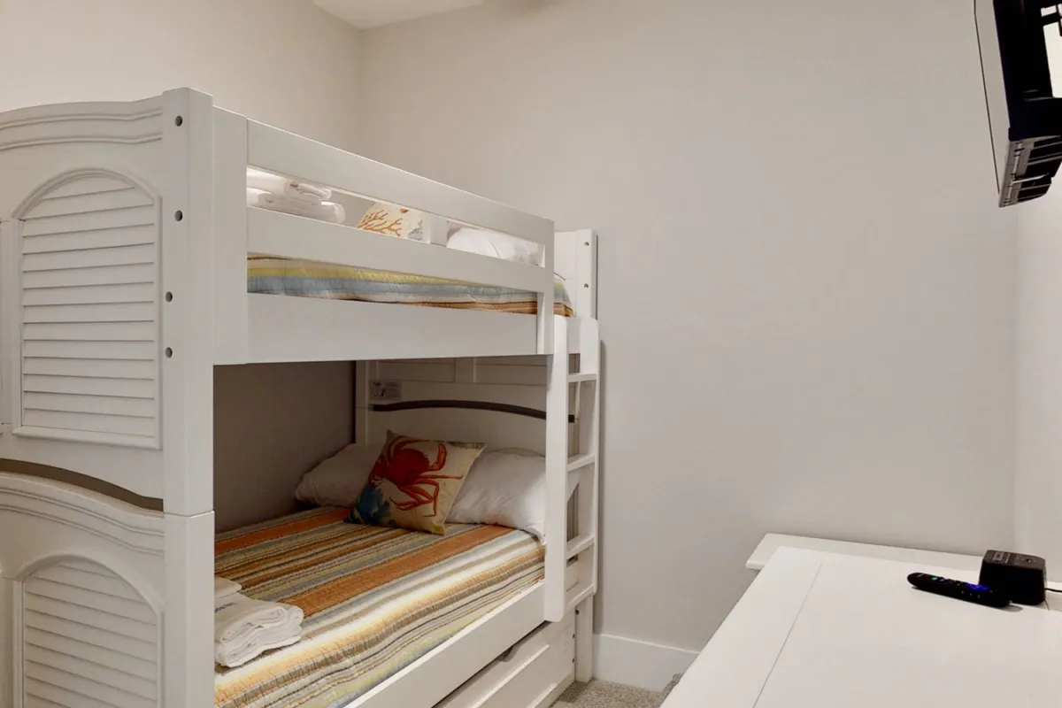A playful and inviting bunk room with sturdy bunk beds, a decorative pillow adding a touch of color, and a television mounted for entertainment. The space feels cozy and tailor-made for kids or groups seeking fun and togetherness.