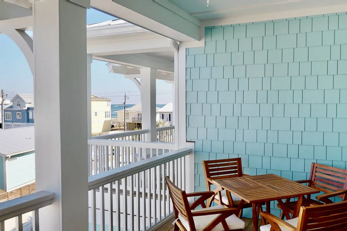 A serene outdoor setting featuring a wooden table and chairs, a shingle wall, and expansive views of the ocean. The arrangement is ideal for enjoying coffee, reading, or hosting outdoor meals with the sound and sight of the sea nearby.